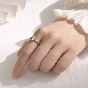 Close-up of golden twisted ring with an oval zircon on a model hand with soft light