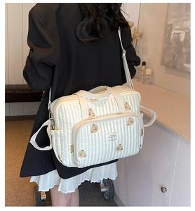 Quilted diaper bag with bear embroidery and adjustable strap shown on model side view