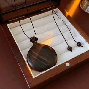 Close-up of a drop-shaped wooden pendant necklace inside a white lined display box