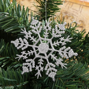 Close-up of sparkling silver snowflake ornament hanging on a lush green Christmas tree