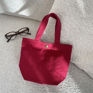 Minimalist burgundy canvas tote bag with metal snap button on a soft white background