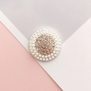 Detail of round charm with white pearls and champagne rhinestones on pink and grey background