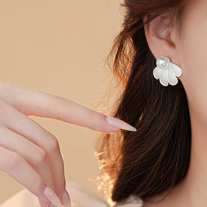 Macro detail of white petal-shaped shell earrings with pearls on a model ear