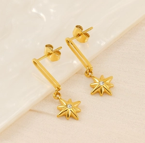 Macro detail of gold-plated star drop earrings with starburst pendant and zircon stone