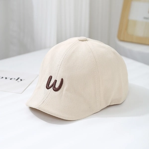Detailed close-up of beige cotton beret with embroidered letter W on white table