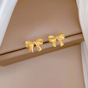 Macro view of gold bow-shaped stud earrings resting on brown box and white silk