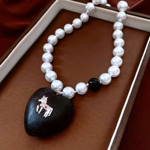 Detail of vintage pearl necklace featuring black heart pendant with silver pony motif