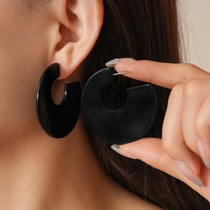 Close-up of a model wearing large black acrylic C-shaped earrings with a minimalist design
