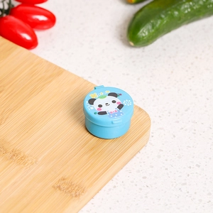 Blue mini sauce container with cartoon panda lid on a wooden cutting board