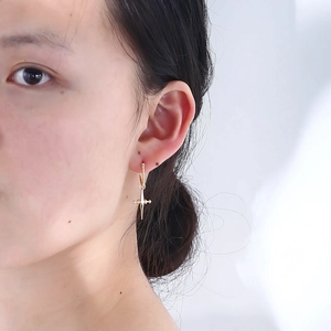 Close-up of gold cross drop earring worn by a model against a white background