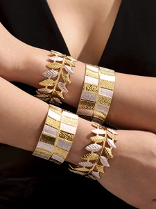Dettaglio dei bracciali a foglia bicolore e polsini dorati strutturati indossati da una modella