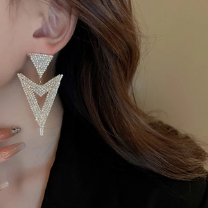 Close-up of a glamorous gold V-shaped earring with shimmering white rhinestones on a model
