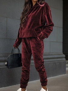 Side view of woman wearing burgundy velvet tracksuit with hoodie and joggers in street setting