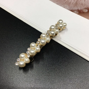 Elegant gold hair clip with white pearls and rhinestones on a minimalist background