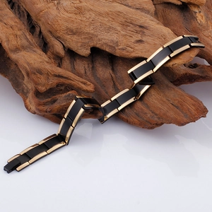 Detail of men's titanium steel link bracelet in black and gold on a textured wood surface