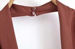 Detail van de achterste halsopening met dubbele knoopsluiting op de roodbruine jurk