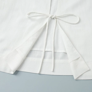 Detail of white cotton-linen fabric featuring a lace-up bow and clean hemline stitching