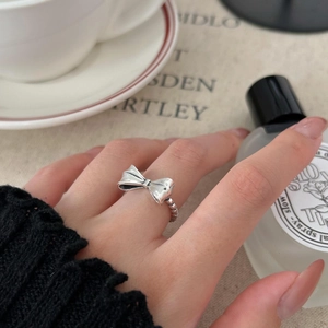 Detail of 925 sterling silver bow ring with beaded texture on a hand in a tea setting