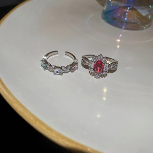 Close-up of silver zircon rings with oval red gemstone and multicolor crystal accents