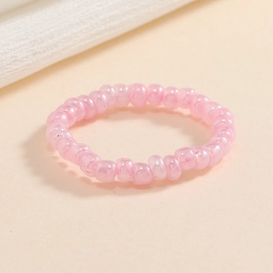 Dettaglio dell'anello elastico con perline rosa lucide su uno sfondo beige neutro