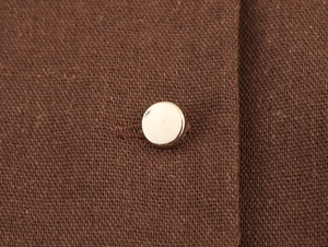 Detailed close-up of dark brown linen-textured fabric with a polished silver metal button