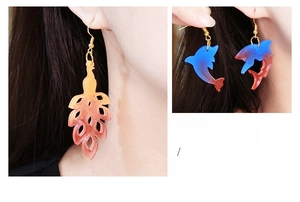 Detail showing gradient feather and dolphin resin earrings worn and held by hand