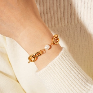 Macro detail of a gold-plated link chain bracelet with a single freshwater pearl on wrist