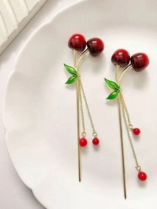 Detail of red cherry hair stick with gold tassels and green leaves on white plate