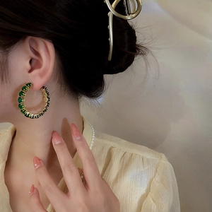 Close-up of golden geometric hoop earrings with green zircon stones on a female model