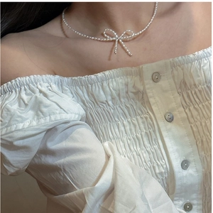 Detail of elegant pearl bow necklace on model wearing a white ruffled top