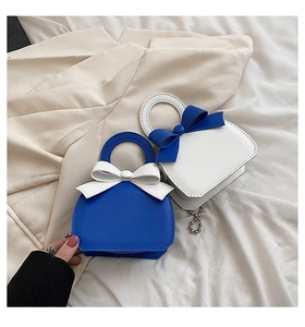 Close-up of mini handbag with bow decoration and metal chain on soft cream background