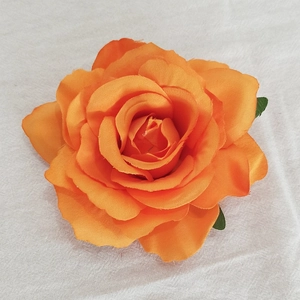 Top view of a single orange fabric rose head with green leaves on white texture