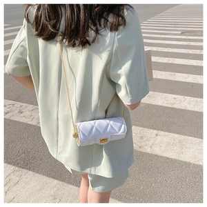 Crossbody view of white quilted cylinder bag with gold chain strap on a model