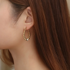 Detailed side view of gold-tone beaded hoop earrings with a single clear gemstone drop