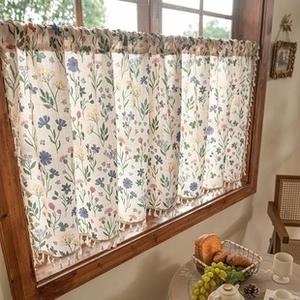 Close-up of floral cafe curtain with delicate tassel trim on a wooden window frame