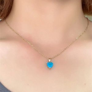 Close-up of a gold heart necklace with a blue gemstone worn by a model for a stylish look
