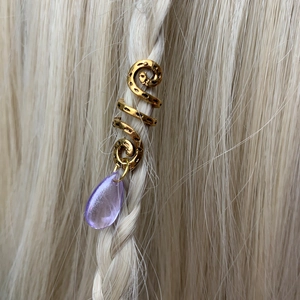 Detailed view of a gold spiral hair charm with purple teardrop bead on blonde braids