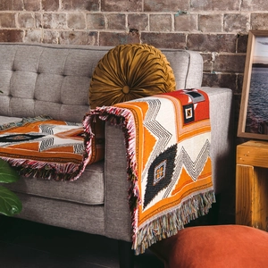 Bohemian geometric picnic blanket with orange and red tones and tassels on a sofa