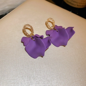 Macro detail of elegant purple petal earrings with textured golden circles on beige leather