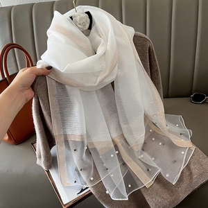 Close-up of white silk scarf featuring gold trim and elegant faux pearl embellishments