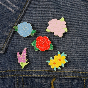 Detailed arrangement of five colorful enamel flower brooches on blue denim fabric