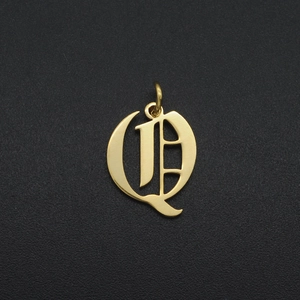Detail of gothic letter Q pendant in gold finish over a textured black background