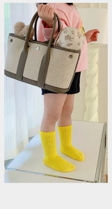 Detail showing bright yellow knitted kids socks paired with a beige canvas tote bag