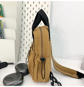 Detail shot of khaki nylon backpack side featuring black handles and drawstring adjustment