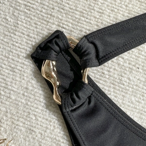Close-up of golden irregular hardware on black cutout one-piece swimsuit shoulder strap