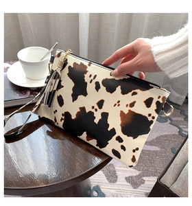 Close-up of cow print envelope clutch with fringe tassel on a wooden table setup