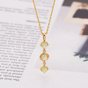 Λεπτομέρεια χρυσού κολιέ με τρεις κάθετους ανοιχτοπράσινους πολύτιμους λίθους
