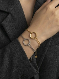 Macro detail of gold and silver geometric rings with double-chain bracelet on grey blazer