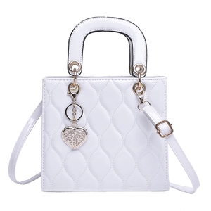 Detailed view of white patent leather handbag with quilted wavy stitching and heart charm