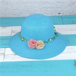 Detail of blue woven straw sun hat featuring decorative green leaf vine and chiffon flowers